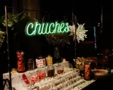Una mesa de chuches para una boda rústica, con un letrero de neón "Chuchés", frascos de dulces, piruletas y decoración invernal.