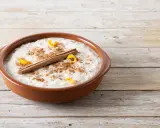 Un tazón de arroz con leche cremoso, espolvoreado con canela y adornado con cáscara de naranja y una rama de canela.