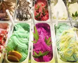 Variedad de helados cremosos, incluyendo un vibrante helado de pitahaya con azúcar invertida, decorado con hojas verdes y frutos rojos.
