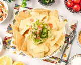 Nachos con queso cubiertos de guacamole y pico de gallo, listos para disfrutar.