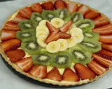 Deliciosa tarta con decoración de tartas con frutas: fresas, kiwi y plátano, dispuestas en círculos concéntricos sobre una base cremosa.