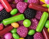 Un surtido vibrante de chuches, mostrando cómo se hacen las chuches con formas de bayas, bastones y pastillas en tonos rojos, verdes, morados y amarillos.