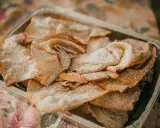 Orejas de carnaval espolvoreadas con azúcar glas en una bandeja metálica. ¡Perfectas para tu receta!