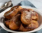 Un plato blanco lleno de torrijas españolas doradas y espolvoreadas con azúcar y canela.