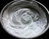 Merengue italiano recién batido en un bol metálico, con remolinos suaves y sedosos que invitan a probar su dulzura.