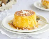 Delicioso flan de coco con caramelo líquido y coco rallado, servido en un plato blanco con una cuchara dorada.