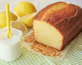 Un delicioso bizcocho de yogur casero, dorado y esponjoso, acompañado de limones frescos y un vasito de yogur.