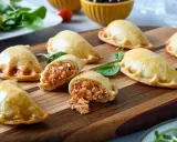 Empanadillas caseras doradas y crujientes, una rellena muestra su sabroso interior. Perfectas para compartir.