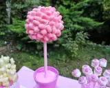 Un árbol de gominolas rosa, decorado con dulces, preside una mesa de fiesta al aire libre.