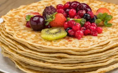 Pila de crepes dorados cubiertos con frutas rojas, fresas y kiwi. Una deliciosa receta crepes para disfrutar.