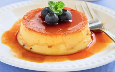 Delicioso flan de queso con cuajada, cubierto de caramelo líquido y adornado con arándanos y menta.