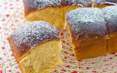 Pan brioche esponjoso y dorado, espolvoreado con azúcar glas sobre una rejilla.