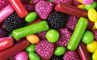 Un surtido vibrante de chuches, mostrando cómo se hacen las chuches con formas de bayas, bastones y pastillas en tonos rojos, verdes, morados y amarillos.