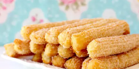 Montón de churros dorados espolvoreados con azúcar, perfectos para aprender como hacer churros caseros.