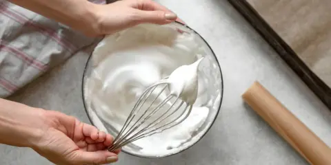 Manos batiendo claras a punto de nieve para un merengue suizo perfecto.