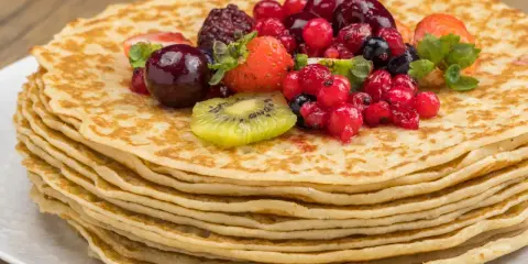 Pila de crepes dorados cubiertos con frutas rojas, fresas y kiwi. Una deliciosa receta crepes para disfrutar.