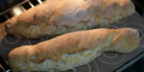 Dos panes dorados recién horneados, hechos con la ayuda de la Thermomix, reposan sobre una bandeja en el horno.