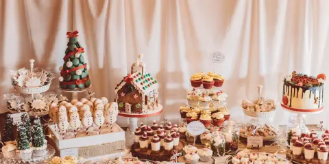 Mesa de dulces navideños con galletas de muñeco de nieve, casa de jengibre, pastel de árbol y cupcakes.