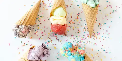 Cinco conos de helado de chuche de colores vibrantes, esparcidos con confeti sobre fondo blanco.
