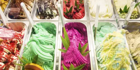 Variedad de helados cremosos, incluyendo un vibrante helado de pitahaya con azúcar invertida, decorado con hojas verdes y frutos rojos.