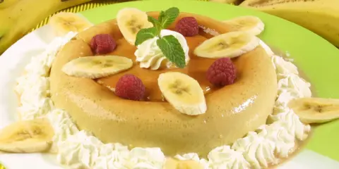 Delicioso flan de plátano adornado con rodajas de plátano, frambuesas y crema batida. Un postre perfecto para cualquier ocasión.