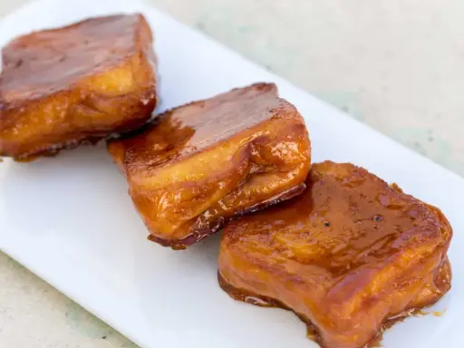 Tres torrijas de miel, doradas y brillantes, reposan en un plato blanco.
