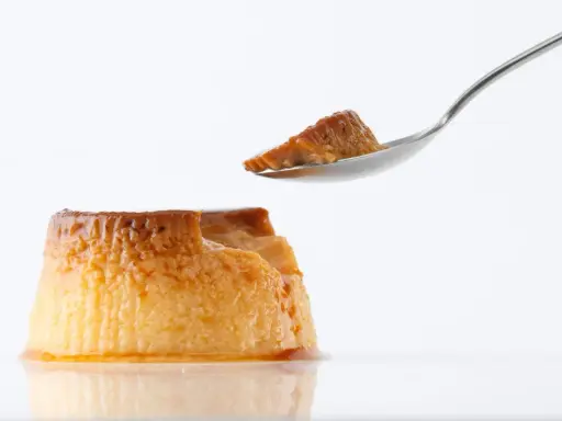 Un trozo de flan casero sin horno en una cuchara, con el resto del postre caramelizado al lado.