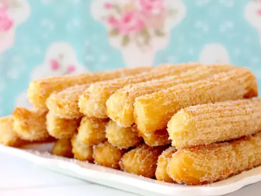 Montón de churros dorados espolvoreados con azúcar, perfectos para aprender como hacer churros caseros.