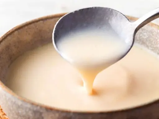 Cuchara sirviendo crema inglesa espesa y suave en un cuenco rústico.