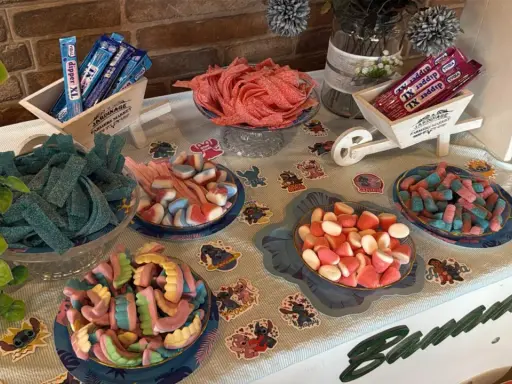Una mesa llena de todas las chuches del mundo: gominolas azules, rojas, rosas y de muchos colores, dispuestas en cuencos y carretillas.