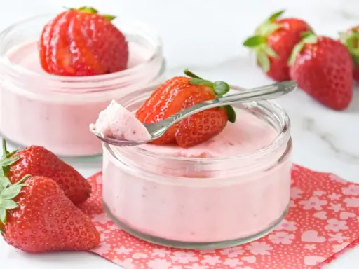 Delicioso postre con fresas, cremoso y ligero, servido en frascos de vidrio. Una fresa fresca corona cada porción.