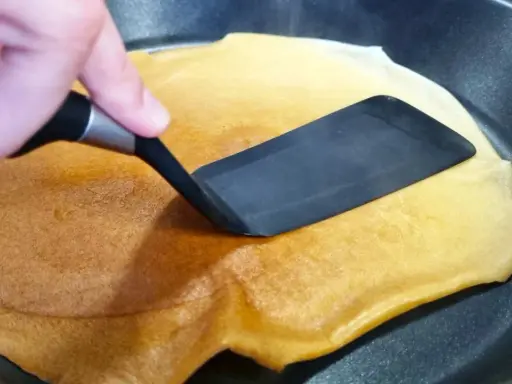 Volteando un crepé dorado en una sartén, preparado fácilmente con crepes thermomix.