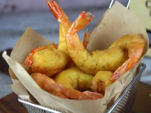 Crujientes gambas a la gabardina doradas, servidas en una cesta metálica con papel marrón.