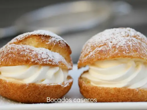 Dos bocados caseros de pasta choux, rellenos de crema batida y espolvoreados con azúcar glas.