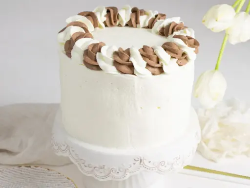 Tarta blanca con borde de nata y chocolate, lista para celebrar.