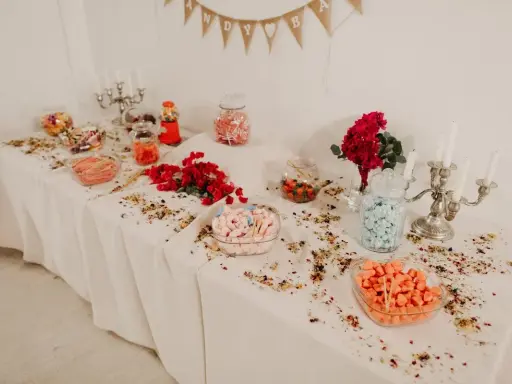Elegante candy bar boda con dulces de colores, flores rojas y candelabros plateados.