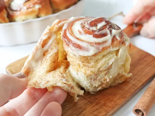 Un rollo de canela esponjoso, cubierto de glaseado cremoso, se separa suavemente.
