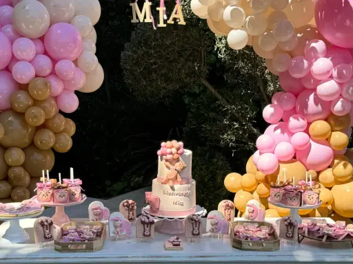 Mesa dulce baby shower con pastel de osito, galletas temáticas y globos rosas y dorados. ¡Bienvenida Mia!