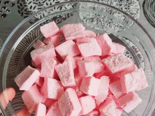Nubes de golosina rosas cortadas en cubos en un bol de cristal, perfectas para recetas dulces.