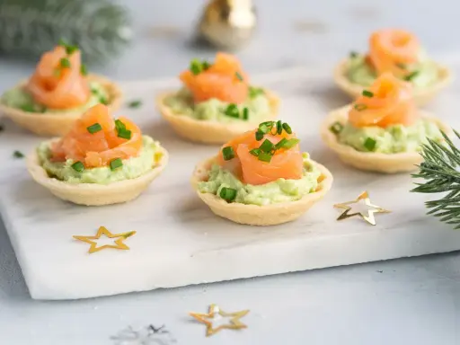 Aperitivos baratos para mucha gente: canapés de salmón y aguacate, decorados con cebollino y estrellas doradas.