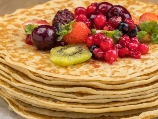 Pila de crepes dorados cubiertos con frutas rojas, fresas y kiwi. Una deliciosa receta crepes para disfrutar.