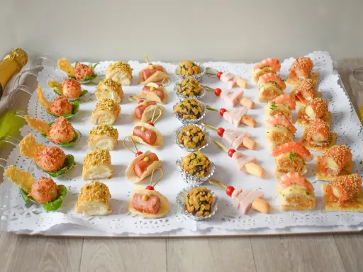 Bandeja con variedad de bocaditos salados, perfectos para un picoteo fácil y económico. Hay mini tacos, bolitas cubiertas de frutos secos, brochetas de jamón y canapés con gambas y salmón.