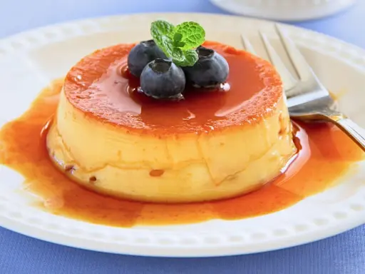 Delicioso flan de queso con cuajada, cubierto de caramelo líquido y adornado con arándanos y menta.
