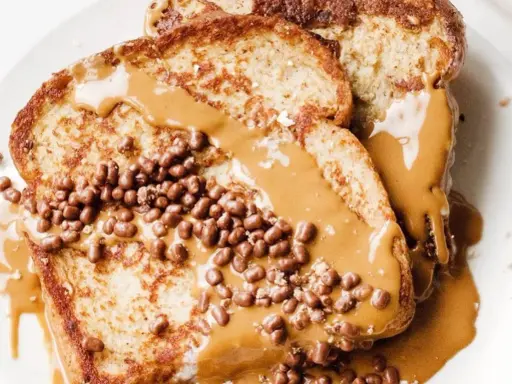 Tostadas francesas cubiertas con crema de cacahuete y crujientes bolitas de chocolate. Un desayuno delicioso y tentador.