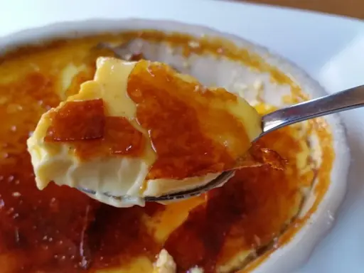 Cuchara levanta un trozo de cremoso creme brulee con su crujiente capa de caramelo tostado.