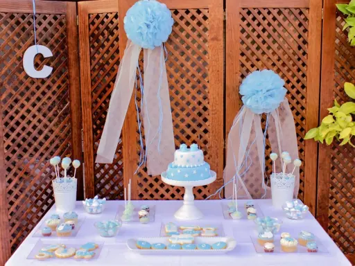 Mesa dulce bautizo casera con pastel, galletas y cupcakes decorados en tonos azules.