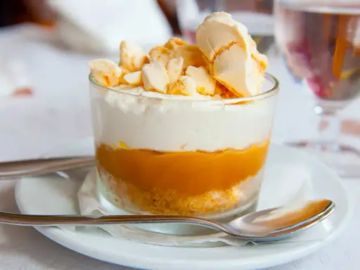 Postre en vaso con capas de galleta, crema y mermelada de mango, coronado con merengue crujiente, como un polvito canario.