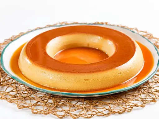 Un delicioso flan de café, con su caramelo dorado, reposa en un plato blanco con borde azul, sobre una esterilla tejida.