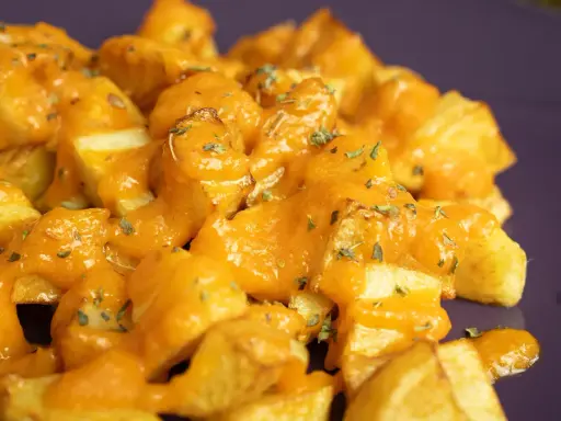 Patatas bravas receta: patatas fritas crujientes cubiertas con una salsa brava cremosa y hierbas picadas.