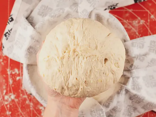 Masa de pan de patata esponjosa, lista para hornear, cubierta con un paño decorado.